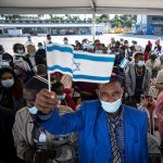 An Ethiopian man waves an Israeli flag as he and other olim enter Ben Gurion Airport (Credit: Olivier Fitoussi, courtesy of The Jewish Agency for Israel)