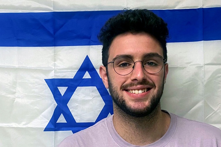 Ofek, a Shaliach, stands in front of an Israeli flag
