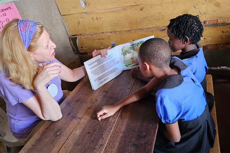 Cindy, a volunteer, reading with two young Ugandan students