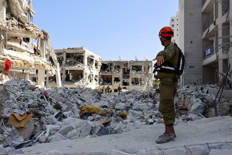 Israeli soldier standing next to building ruined by Iranian missiles.