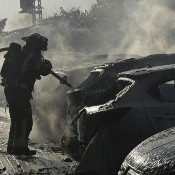 A firefighter hoses down a car after a missile attack